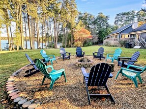 Inviting fire pit area with turquoise chairs surrounded by trees and overlooking a peaceful lake, perfect for cozy gatherings
