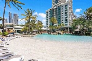 Step into the first pool, a sun-drenched oasis with ample loungers nestled in soft sand. This expansive pool stretches wide, offering endless water to cool off in and plenty of space to soak up the sun.