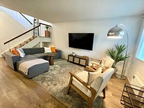 Living room with large sofa, 2 accent chairs, 65" TV, & games.