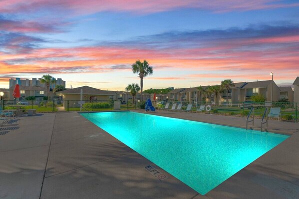 A stunning view of the community pool area lit up at night, with sitting lawn chairs nearby, creating a peaceful and inviting atmosphere for evening relaxation.