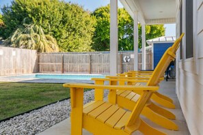 A cozy fenced backyard with a sparkling pool and cheerful bright chairs!