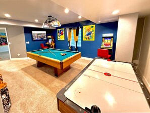 An entertainment haven featuring a pool table, two arcade machines, an air hockey table, and a Smart TV—perfect for endless fun and relaxation
