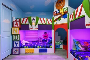 A whimsical Toy Story-themed bedroom with four twin beds, a private en suite bathroom with a shower, and a smart TV.