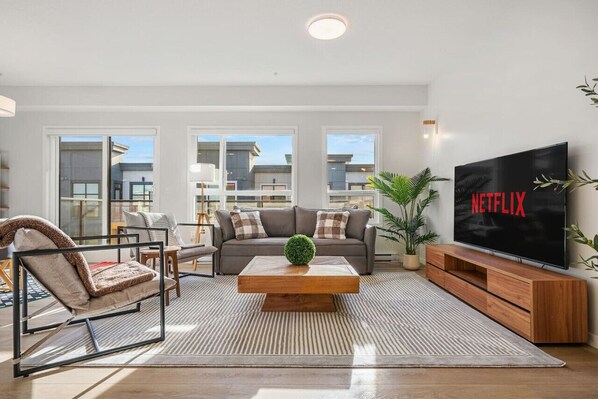 Living room featuring a 70" TV with Netflix, 2 Person Queen Sofa Bed & Tons of natural lighting. AC Inlcuded.