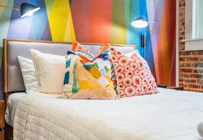 The queen bed is cozy and inviting, with colorful pillows and soft bedding creating a relaxing space to recharge after a busy day.