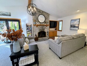 The cozy living room features a stunning stone wood-burning fireplace and a wall-mounted TV