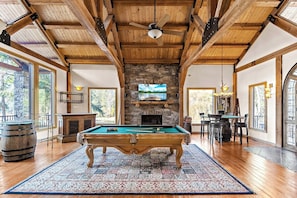 This room also includes a gas fireplace, a bar, a TV, a game table, and multiple seating areas, creating an ideal space for relaxation and entertainment.
