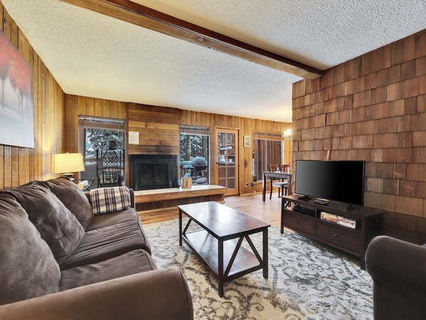 View of the inviting living room featuring comfortable seating, a 55” smart TV, DVD player, and a cozy wood-burning fireplace