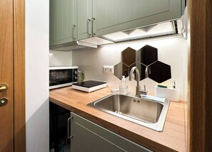  A compact kitchen equipped with all essentials, including a sleek microwave and hotplate. Check availability today!