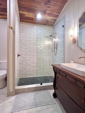 The ensuite master bath with antique vanity, oversized shower, and heated floors