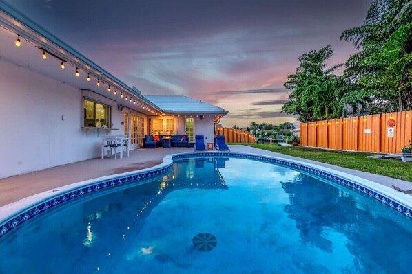 Heated swimming pool, comfortable outdoor sofa seating with firepit, lounge chairs, bean bags outdoor game, and a view of the boat dock.