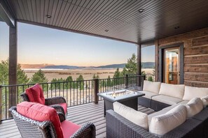 Gather on this expansive covered deck at Trumpeter Swan, offering plush seating around a gas fire pit and breathtaking views overlooking Henry's Lake and distant mountain ranges—perfect for peaceful evenings.