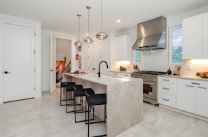 The fully equipped modern kitchen is stocked with all culinary essentials, stainless-steel appliances, and breakfast bar seating. (Main Floor)