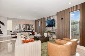 Bright open floor living space featuring a smart flat-screen TV, gas fireplace, and designer furnishings. (Main Floor)