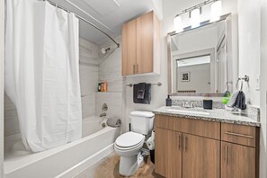 This bright and welcoming bathroom invites you to freshen up in comfort. Enjoy the forest-inspired shower curtain that adds a calming touch to your routine, complemented by the cozy rug underfoot and sparkling clean fixtures.