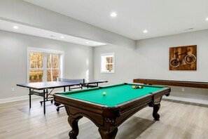 Spacious game room featuring a pool table, ping pong table, shuffle board, and bar seating, perfect for fun and relaxation.