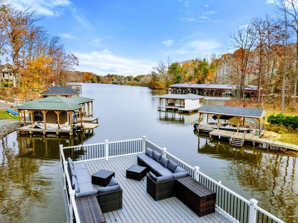 Spacious outdoor deck with comfortable seating, lounge chairs, and scenic views of a wooded area and water.