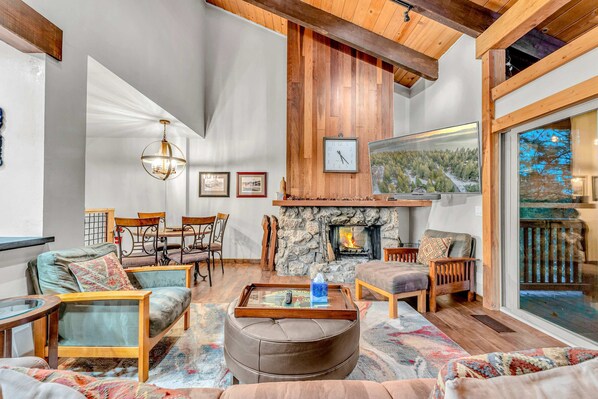 Main living space: Couch, 2 chairs, wood-burning fireplace, 65” Smart TV, 4-person dining table, access to deck with outdoor furniture