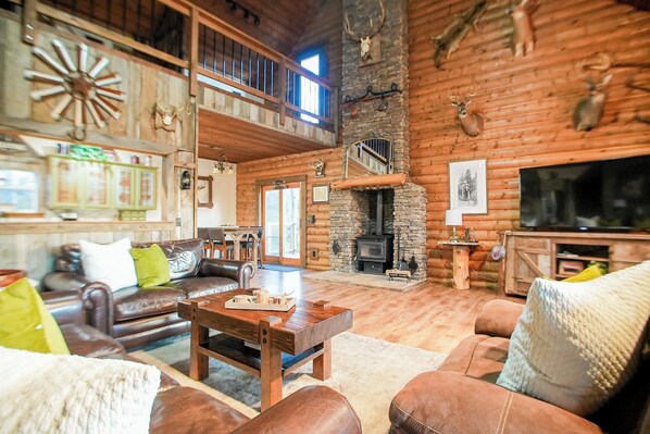 This cozy living space combines stunning wood details with high ceilings and a decorative stone fireplace, adding a charming cabin touch for your family gatherings.