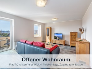 heller, offener Wohnraum mit Flat-TV und Balkonzugang