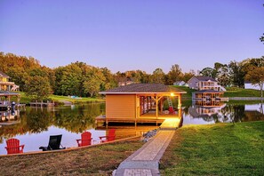 A cozy illuminated dock with Adirondack chairs overlooks a tranquil lake at sunset, creating a peaceful and inviting retreat.