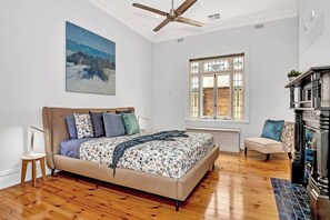 Relax in the spacious primary bedroom, featuring a plush king-sized bed, heritage windows, and a ceiling fan for added comfort. The fireplace is decorative and not available for use. 