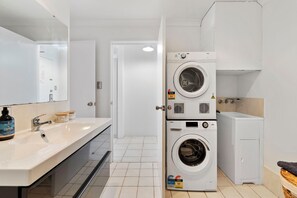 Experience a bright and airy bathroom equipped with a vanity, a refreshing shower, and the convenience of a washing machine and dryer for added functionality.