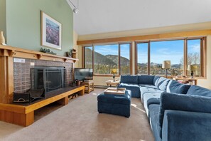 Living room featuring a wood burning fireplace, TV, and large windows filing the room with natural light.