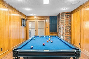Game room with a pool table, dartboard, brick accents, and wood-paneled walls.
