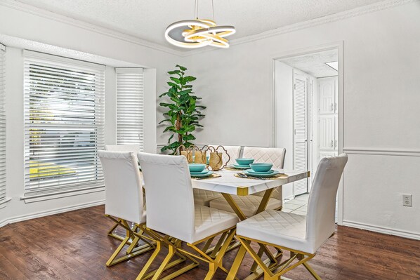 Dining room with white chairs, gold legs, turquoise dishes, a modern chandelier…