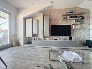 Ce salon moderne est idéal pour recevoir des amis ou regarder un film. Des étagères pour maximiser le rangement. Les luminaires intégrés ou discrets pourraient ajouter une ambiance chaleureuse en soirée. TV plat avec wifi gratuit