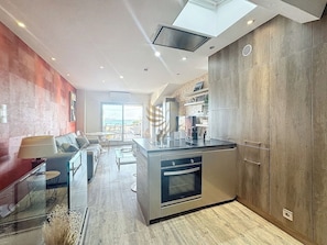 logement moderne, baigné de lumière grâce à sa grande baie vitrée, propose un espace convivial. L'îlot de cuisine est idéal pour la préparation de repas en famille ou entre amis. Imaginez-vous ici, savourant un café matinal avec vue sur la mer.