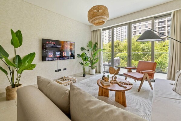 TV on the wall, sofa and chair facing balcony with garden view.