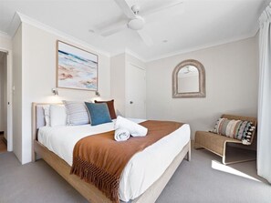 Bedroom #1: It is decorated in a coastal style, with a light and airy feel. The walls are painted in white, and the floor is covered in a neutral carpet. The bed has a wooden frame and is dressed in white linens with a burnt orange throw blanket.