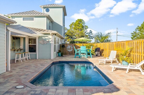 A stunning oasis featuring a sparkling pool, comfortable seating, and a dining space seamlessly connected to the outdoor kitchen and spa for ultimate relaxation and entertainment.