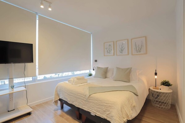 Relax in this serene bedroom with a cozy bed, modern decor, and a wall-mounted TV for your entertainment.