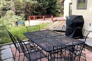 The side patio has a table for six and a propane grill. The large deck and backyard are in the background.