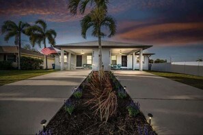 Welcome to your tropical escape! This beautifully lit duplex offers double the charm with spacious driveways, palm-lined landscaping, cozy front seating, and a peaceful sunset backdrop—perfect for evening chats or morning coffee outdoors.