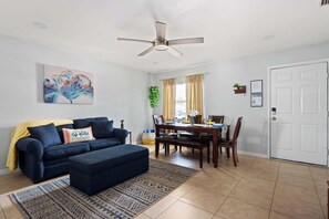 Chic and cheerful, this cozy living and dining area features a comfy navy sofa, stylish ottoman, inviting dining table for six, and warm natural light—perfect for relaxing, sharing meals, or planning your next adventure.