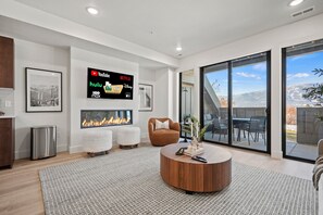 Experience the cozy living room, outfitted with plush seating, a fireplace, an expansive smart TV, and patio doors that frame the breathtaking mountain vistas.
