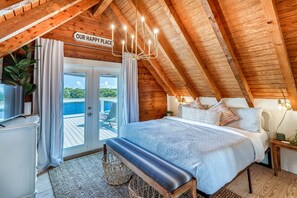 Upstairs bedroom with a king sized bed, a closet, dresser, luggage rack, ceiling fan, & a 32-inch Roku TV. The upstairs bedroom has French doors that lead to a large deck with loungers where y