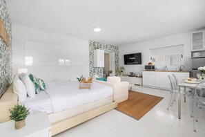 Charming studio apartment with a fully equipped kitchen, dining area, and a cozy bed with soft pillows, all in one convenient space.
