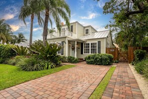 This charming home offers a picturesque brick driveway, surrounded by lush palms and vibrant greenery, creating the perfect getaway atmosphere.
