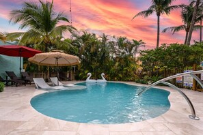 Bask in the warmth of the sun by this serene pool, surrounded by swaying palms, relaxing lounge chairs, and playful swan floats, all under a vibrant sunset sky.