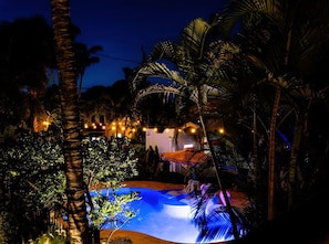 Bask in the enchanting glow of string lights by the pool, surrounded by lush palms for a magical evening retreat.