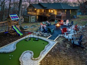 view of the back yard with the firepit with plenty of chairs, mini golf, playset and you can see the house behind with the private hot tub