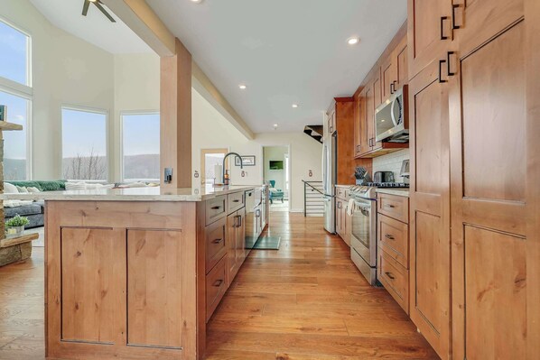 Skalli Haus large kitchen featuring massive island with sunken sink and dishwasher.  Gas stove, convection microwave, french door refrigerator with lower drawer freezer, pantry cabinet with slide out drawers, and Kurig & Drip Coffee