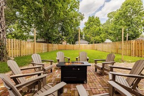 Large fully fenced backyard with brick patio, string lights, and firepit. 