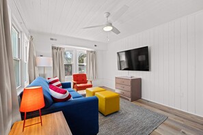 Bright and inviting living space featuring a modern design with vibrant pops of color. Relax on the cozy blue sofa, enjoy the spacious layout, and watch your favorite shows on a sleek wall-mounted TV. Perfect for unwinding after the beach.