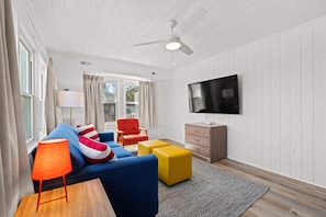 Bright and inviting living space featuring a modern design with vibrant pops of color. Relax on the cozy blue sofa, enjoy the spacious layout, and watch your favorite shows on a sleek wall-mounted TV. Perfect for unwinding after the beach.